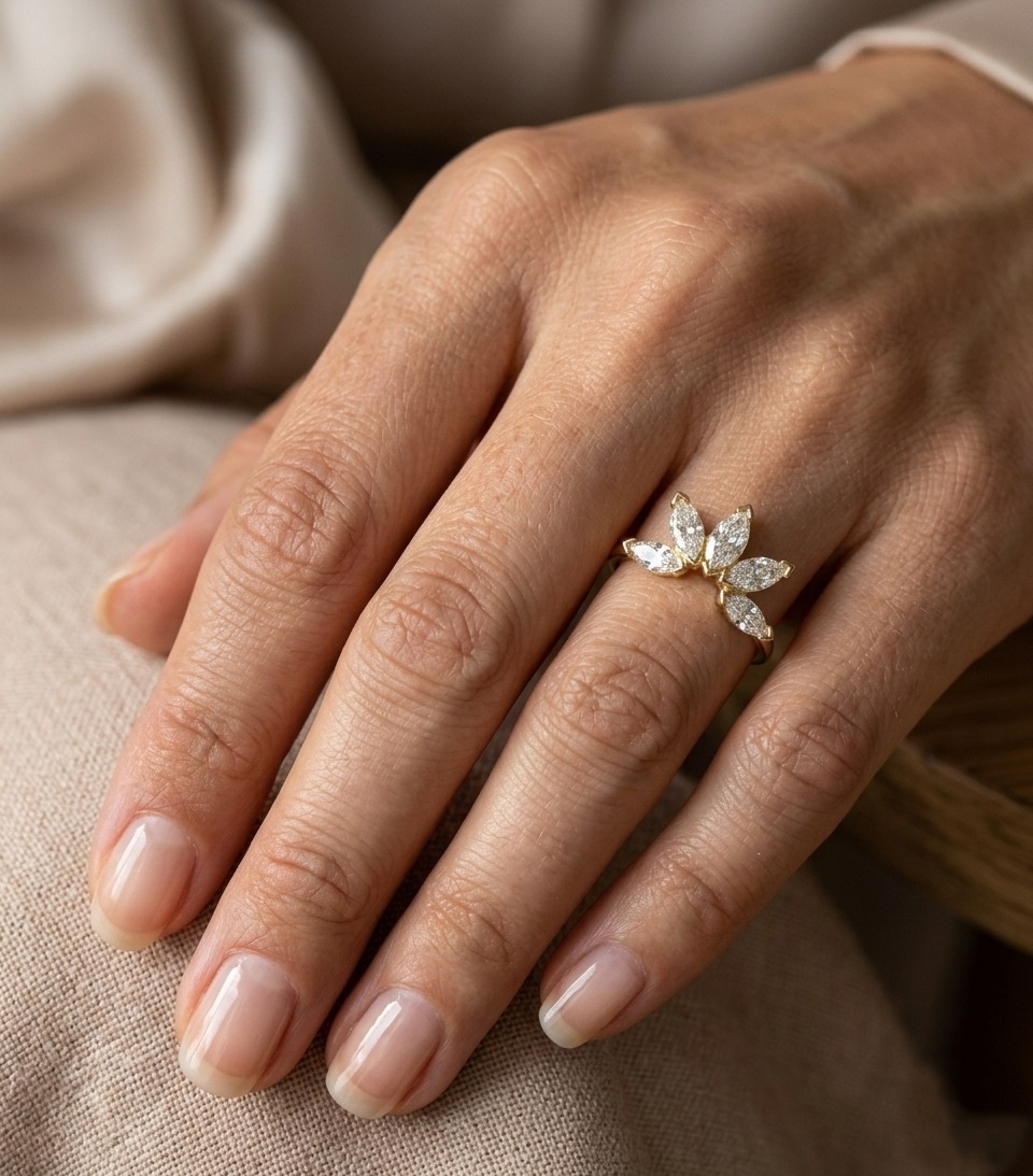 Main portant une bague en or jaune dont les diamants navette s’ouvrent en demi-soleil autour du doigt.